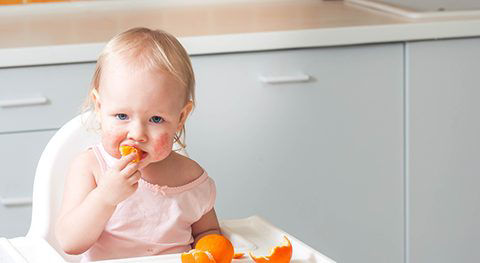 Toddler sitting in a high chair, eating orange slices