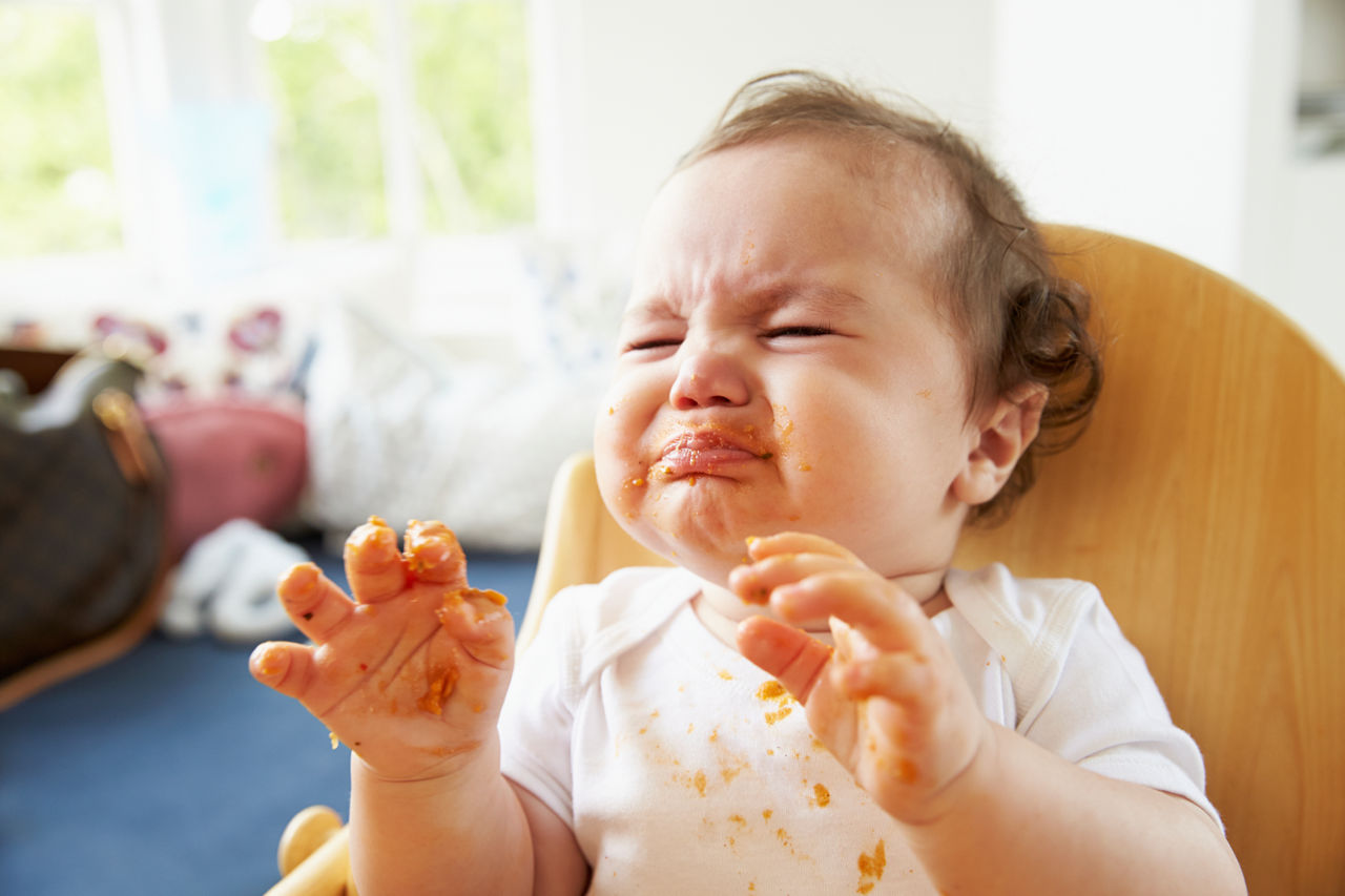 Unhappy Baby In High Chair At Meal Time