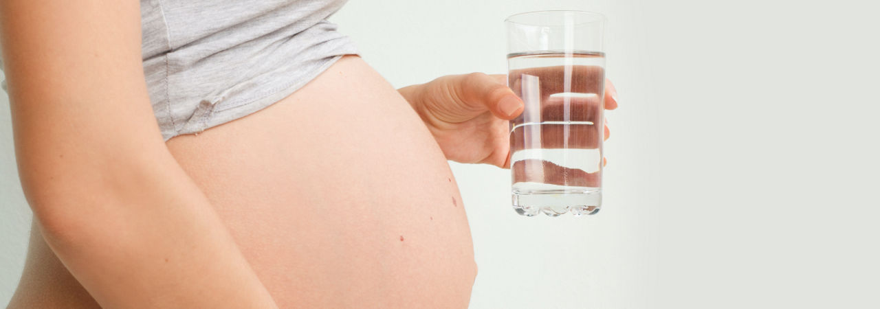 Woman with pregnant belly holding glass of water