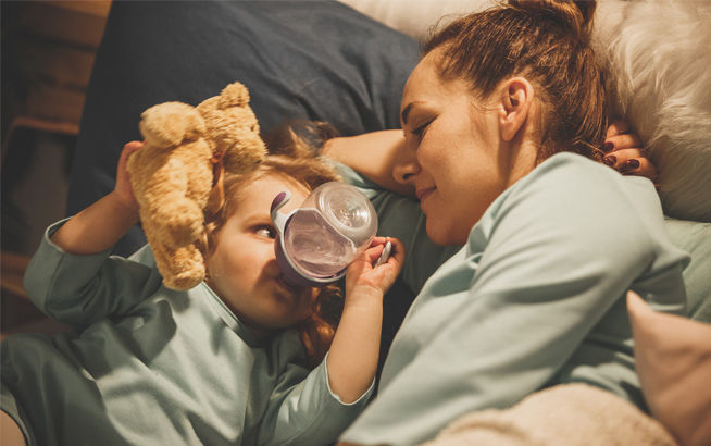 Mamá con niño bebiendo de vaso entrenador acostados y felices