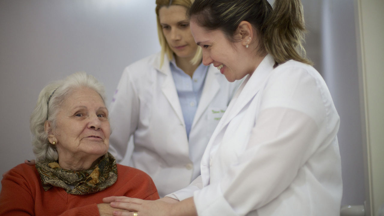 two-smiing-doctors-care-for-older-woman-sitting-down.jpg