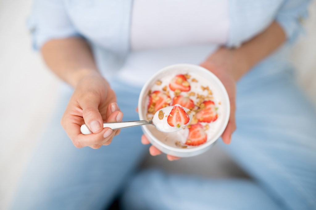 woman holding a bowl with Activia and strawberries
