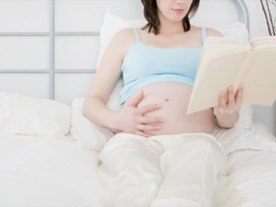 Pregnant woman on bed reading book