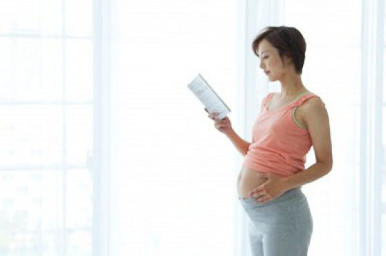Pregnant woman standing and reading a book by the window --- Image by © AID/amanaimages/Corbis