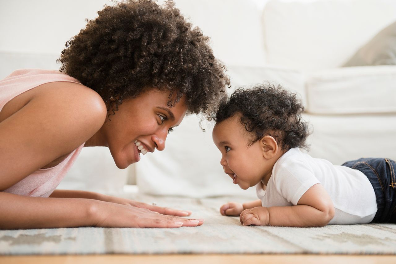 Mother playing face to face with baby son on floor