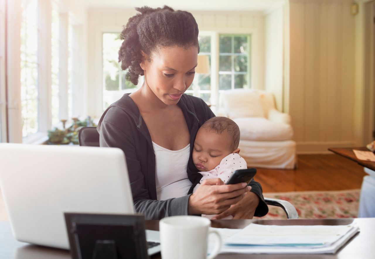 Mother holding baby and working in living room