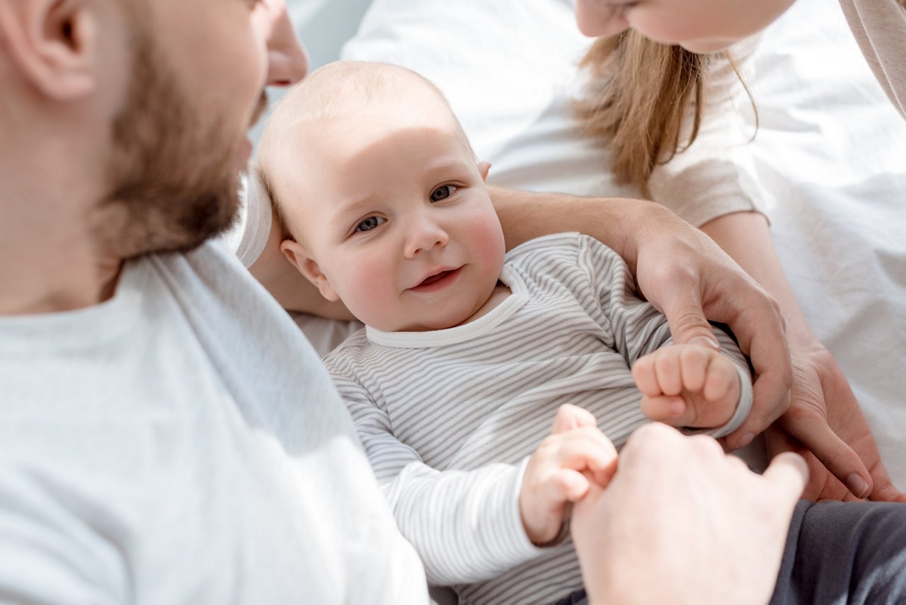 young happy parents with little baby on bed