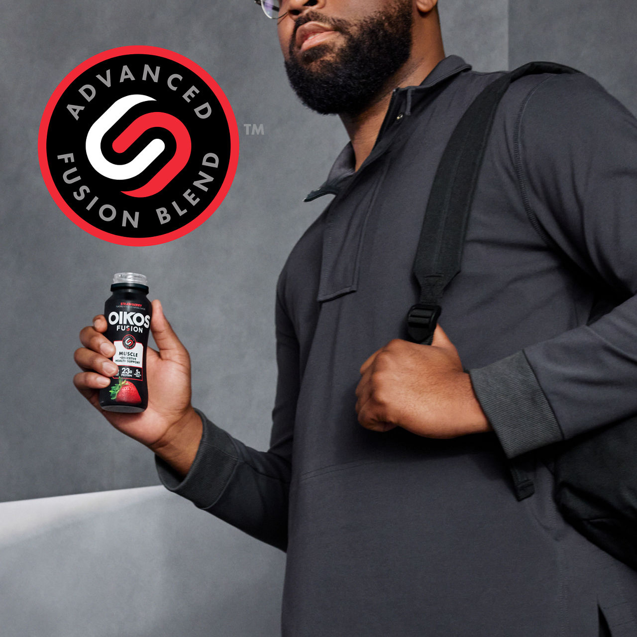 Man dressed in a dark casual outfit holds an Oikos Fusion drink bottle, advanced fusion logo at side