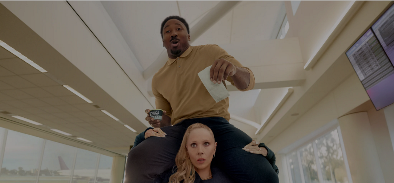 Juno Temple runs in airport, Myles Garrett on shoulders, clutching pass and Oikos Triple Zero cup