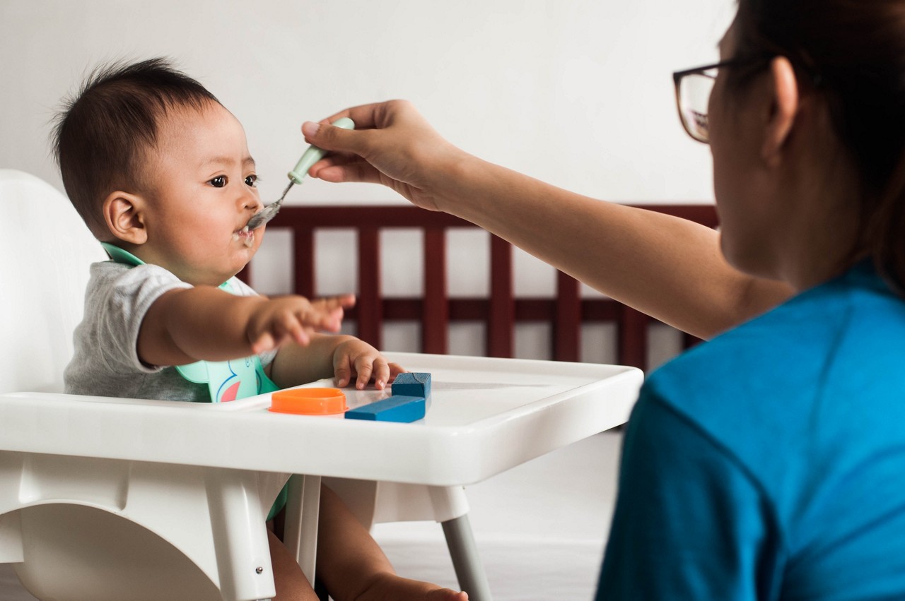 Candid portrait of Southeast Asian mother feeding her baby boy with pureed vegetable